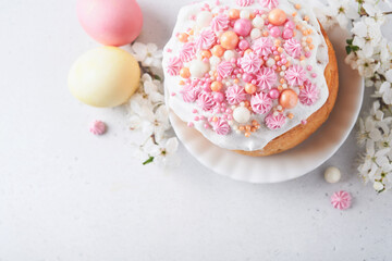 Traditional Easter sweet bread or cakes with white icing and sugar decor, colored eggs and cherry blossom tree branch over white table. Various Spring Easter cakes. Happy Easter day. Selective focus.