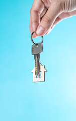 The hand holds a key with a keychain in the form of a house on a blue background