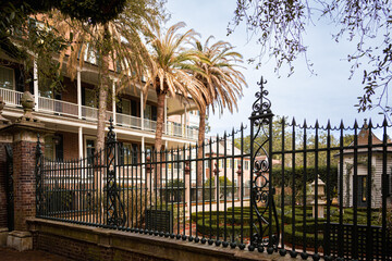 Fototapeta premium Elegant iron fence guarding a traditional southern house and garden with topiaries, Charleston, South Carolina, USA