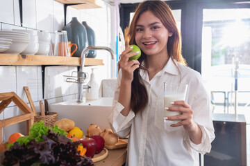 Woman with a beautiful face in a white shirt is making a healthy breakfast with bread, vegetables, fruit and milk inside the kitchen and opening her laptop for cooking lessons. healthy cooking ideas.