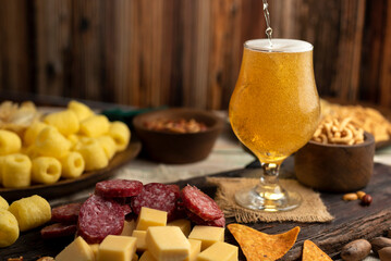 glass of beer with chopped snack chizitos mani chips salami and nachos on wooden table