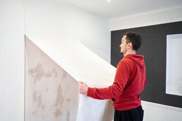 Repair the house with their own hands. The guy is ripping the old wallpaper off the wall