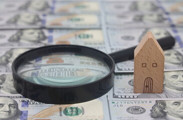 House model and magnifying glass on a background of dollar bills.