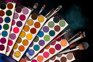 Bright eye shadow, blush brushes, explosion of multicolored powder dust on black background. Highly...