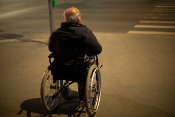 Obraz premium Wheelchair accessible at night. Man in wheelchair for disabled on road.