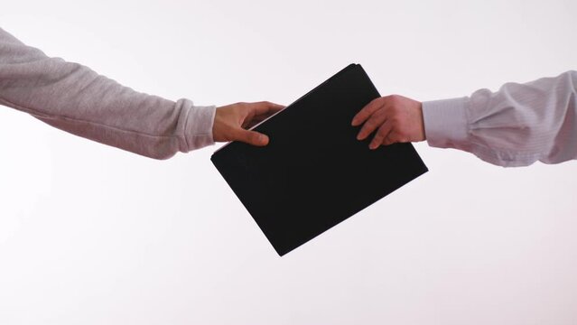 A woman passes a black folder on a white background to a man. A closeup in the frame of only hands and a folder. Transfer of classified information