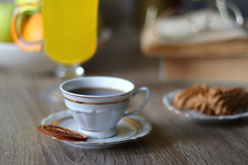 Cup of tea, plates with cookies, glass of orange juice, books, reading glasses, bowl of fruit and candles on the table. Selective focus.
