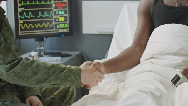 Medium section slow motion of unrecognizable military hospital patient greeting his visitor with handshake