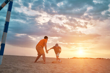 Happy family outdoors, Father and Son playing football, family fun players in soccer in dynamic action have fun playing football in the beach, summer day under sunlight.
