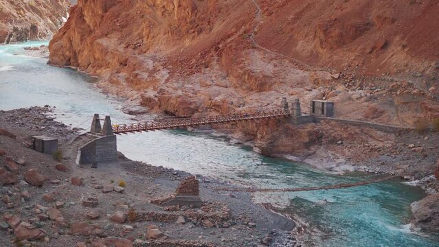 4K shot of old and new foot bridges above the blue Tsarap river flowing in between mountains on the way towards the Phugtal Monastery near Purne village in Zanskar, Himachal Pradesh, India.	