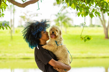 Uma mulher jovem com um cachorrinho no colo em um parque muito arborizado.