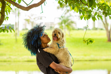 Uma mulher jovem com um cachorrinho no colo em um parque muito arborizado.