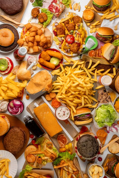 Table full of fast food: hamburgers, fries, cheese balls, burgers, and more. View from above, vertical. Created with Generative AI technology.