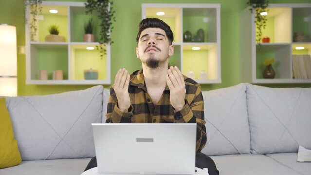 Young entrepreneur man praying while doing business. 
Young man working on laptop finishes his work and prays for his wish to come true.

