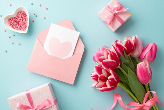 Mother's Day concept. Top view photo of bouquet of tulips present boxes with ribbon bows envelope with postcard and heart shaped saucer with sprinkles on isolated pastel blue background