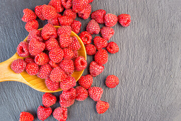 ripe raspberry spilled from a wooden bowl on a gray background