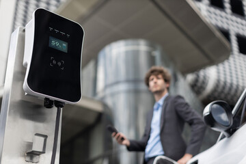 Below view of progressive businessman with electric car recharging at public charging station at...