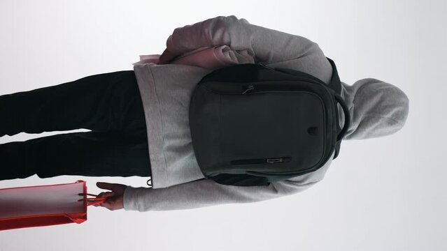 A man in youth sportswear with a backpack and a folder on a white background. Student. Student Practice. Tourism. Expectation. Vertical frame. Back view