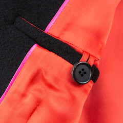 Interior button pocket in black wool coat with bright red lining. Close up
