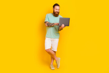 Full body photo of cheerful young man use wireless netbook write email isolated on yellow color...