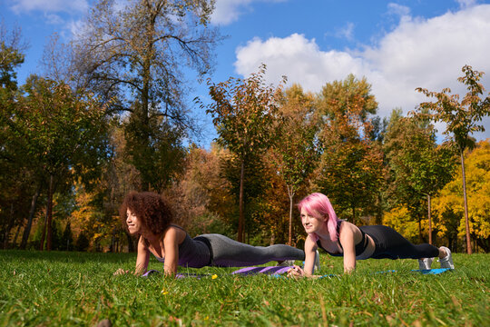 Joyous interracial sportwomen performing isometric core exercise outdoors