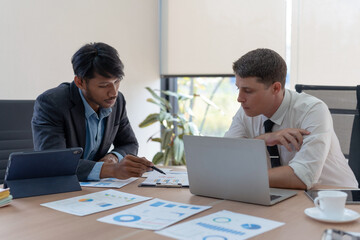 Group of diverse businessman going over paperwork together and working on laptop at meeting.