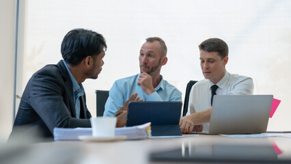 Group of diverse businessman going over paperwork together and working on laptop at meeting.