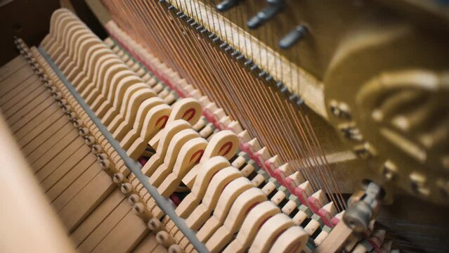 Several piano hammers strike piano strings in an old home piano upright piano made of light wood.