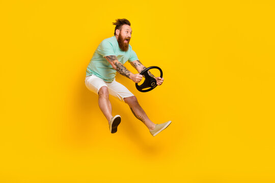 Full body cadre of overjoyed young jump man red hair wear green t-shirt hold steering wheel driving fast speed new car isolated on yellow background