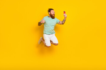 Fototapeta na wymiar Full body photo of jump popular blogger irish tattooed man thumb up recording video take selfie hold smartphone isolated on yellow color background