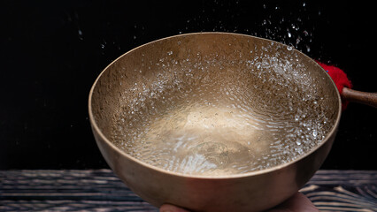 Drops of water fly into the air from hitting a Tibetan (singing) bowl. Cold boil. Tibetan bowl on a...