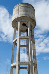 water tank seen from below and silhouetted against a blue sky with clouds
