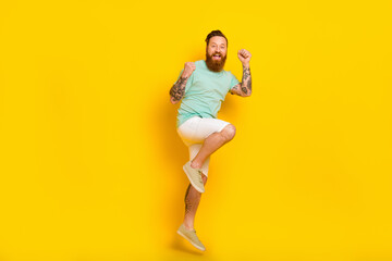 Fototapeta na wymiar Full length size photo of energetic young red hair guy tattooed businessman fists up jumping celebrate success isolated on yellow color background