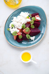 Turquoise plate with beetroot, grapefruit and feta cheese salad, vertical shot on a light-beige marble background, high angle view