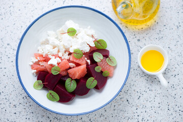 Plate of salad with beetroot, feta cheese and grapefruit, horizontal shot on a light-grey granite background, elevated view