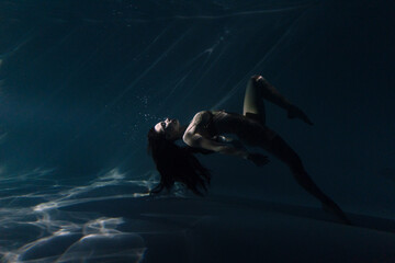 Underwater shoot of beautiful woman with long hair dancing in water in sunbeams.