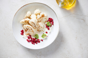 Plate with fried cauliflower florets and pomegranate seeds, top view on a light-beige stone background, horizontal shot with space