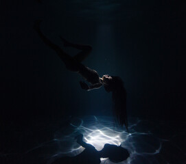 Fototapeta na wymiar Underwater shoot of beautiful woman swimming and relaxing in water in sunbeams.