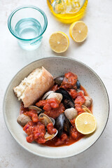 Plate of tomato broth with mussels and vongole clams, vertical shot on a light-beige stone background, elevated view