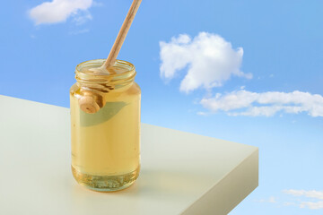 Glass jar with golden-yellow organic, raw honey and wooden honey stick dipper on beige table....