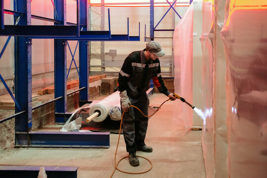 Factory worker packing goods by film using blowtorch