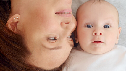 Happy newborn baby with his mother. Healthy newborn baby in a white t-shirt with mom. Closeup Faces of the mother and infant baby. Cute Infant boy and parent, top view. Happy family portrait