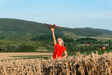 Happy blond boy with toy plane in wheat field on mountains background. Flights and travel with children.