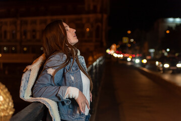 Fototapeta na wymiar Portrait of young brunette woman on bridge on night city backdrop. Stylish girl on night city street.