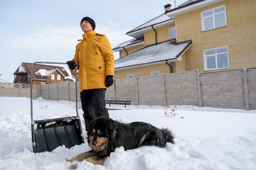 Man removing snow from sidewalk after snowfall. Portrait of man with dog during winter time