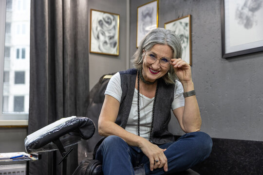 Grey-haired woman sitting on couch in the tattoo salon