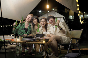 Group of diverse ethnicity young people enjoy eating and grilling bar-b-q together while camping in forest at night.