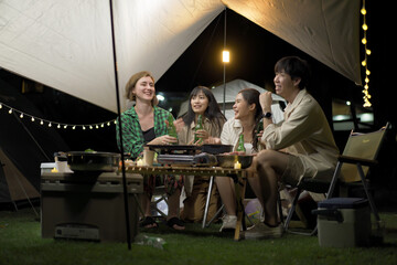 Group of diverse ethnicity young people enjoy eating and grilling bar-b-q together while camping in...