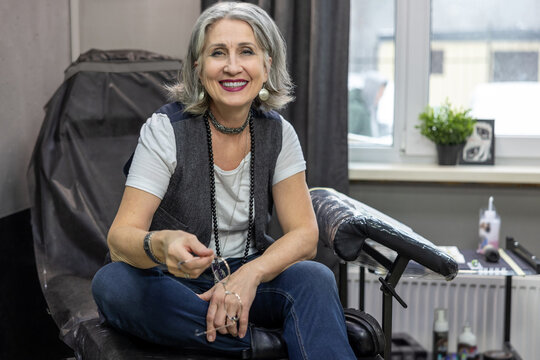 Grey-haired woman sitting on couch in the tattoo salon