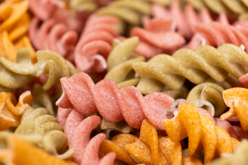 Rice vegetable pasta in the form of spirals, top view. Healthy rice pasta with tomatoes, selenera, carrots and beets